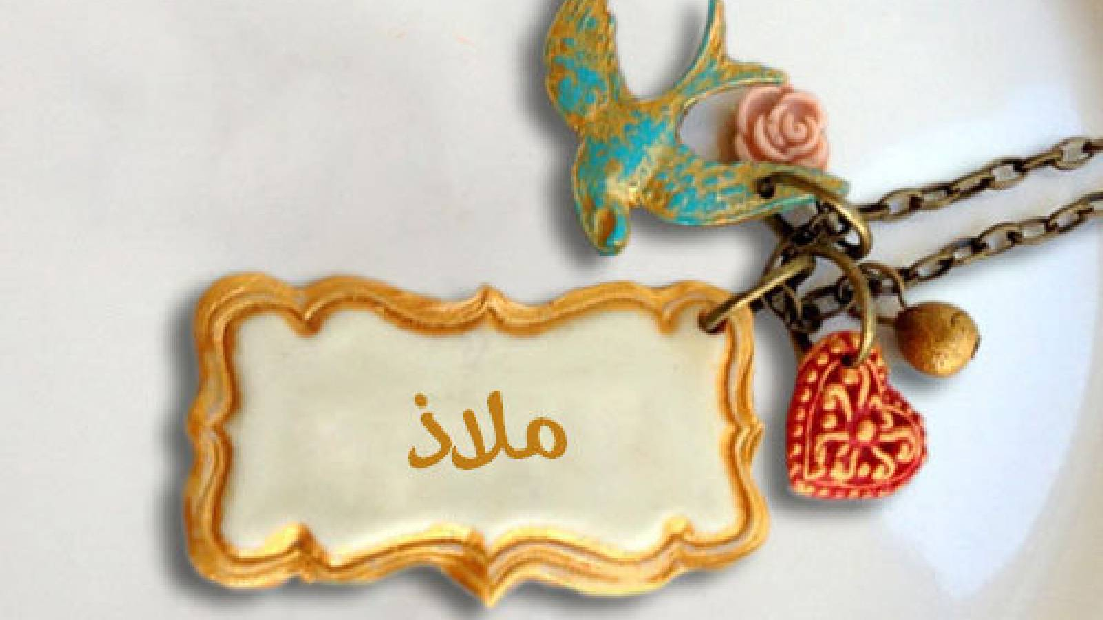 على خلفية بيضاء تظهر قلاده فيها قلب احمر و عصفور وقطعة مستطيله وفي الوسط مادة بيضاء مكتوب عليها اسم ملاذ