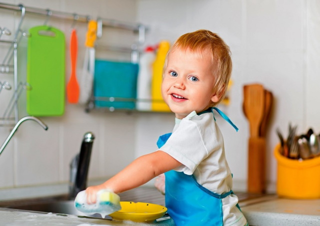 طفل صغير يقف على المجلى يساعد في الجلي واعمال المنزل 