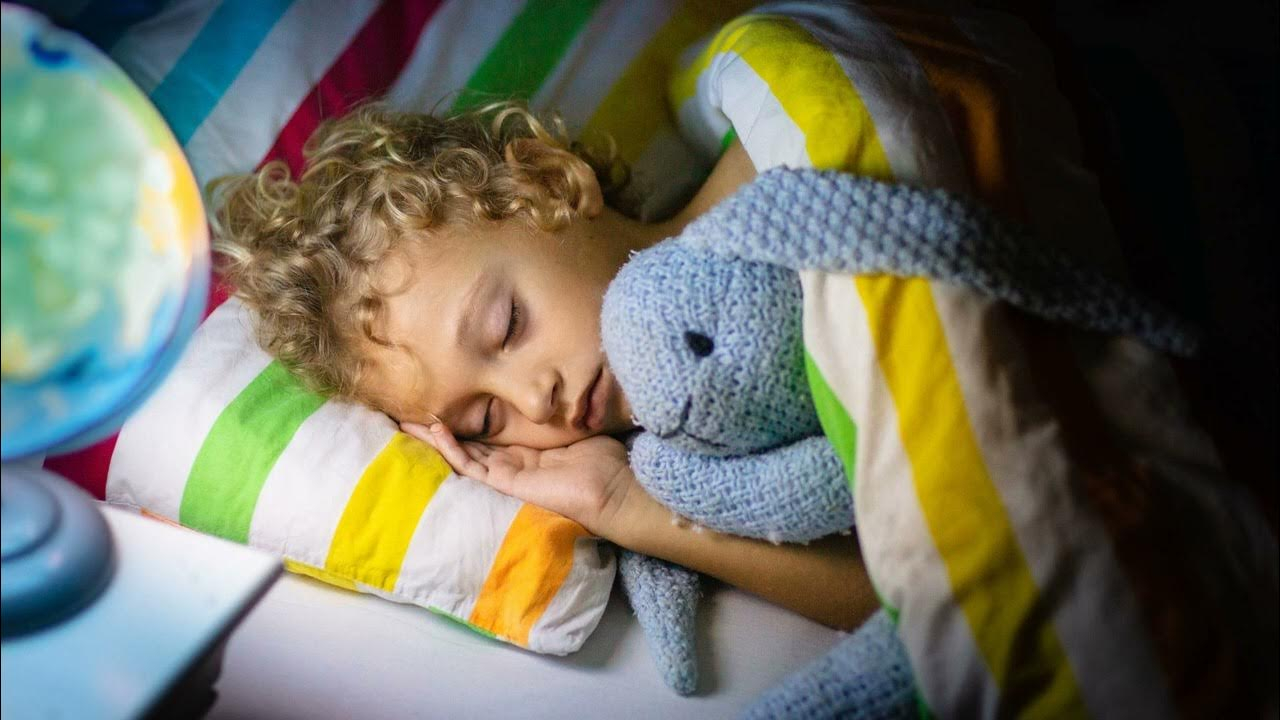 طفل ينام في سريره على وسادة مخططة و هو يحتضن لعبته على شكل ارنب 