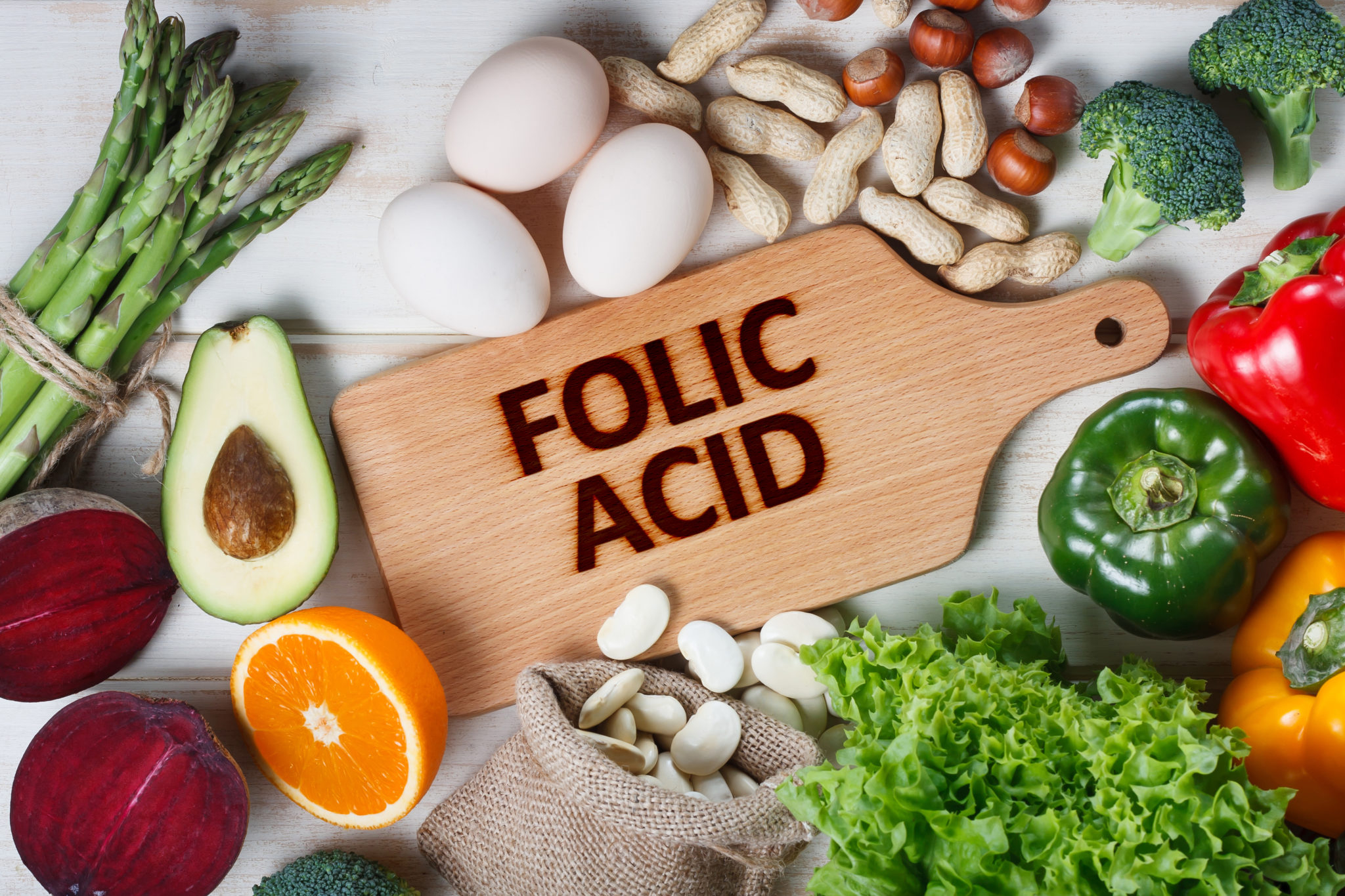 حمض الفوليك لوح للتقطيع من الخشب مكتوب عليه FOLIC ACID وحوله الكثير من الخضار والفواكه من الفليفلة و الليمون والبيض و الشمندر و غيرها