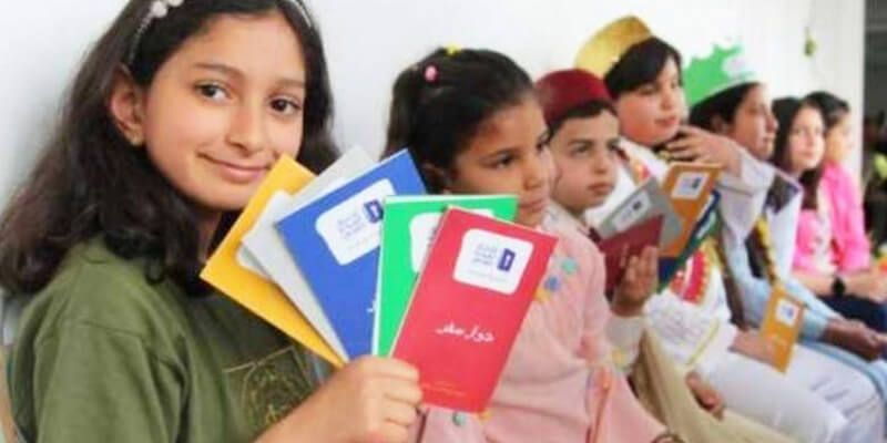 مجموعة من الاطفال المشاركين في تحدي القراءة العربي وتحمل الطفلة الاولى مجموعة من الكتب يظهر عليها شعار المسابقة 