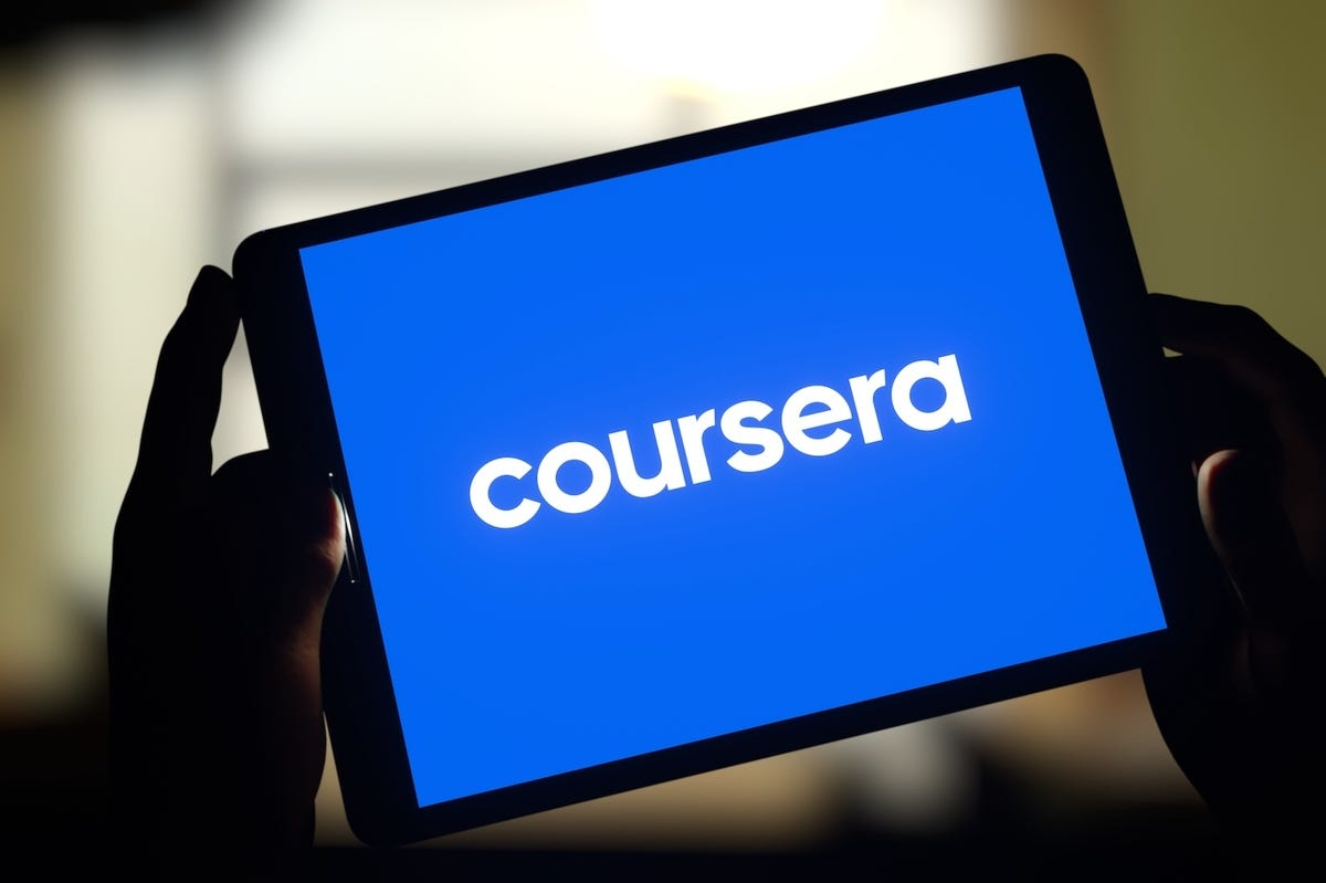 يدين تمسكان بتاب تظهر على شاشته الزرقاء عبارة coursera