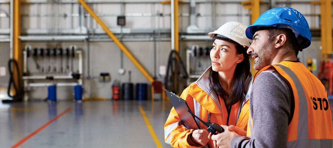 في بيئة عمل يظهر عاملين وهما يرتديان لباس خاص بالعمل و يضعون خوذتين للسلامة المهنية 