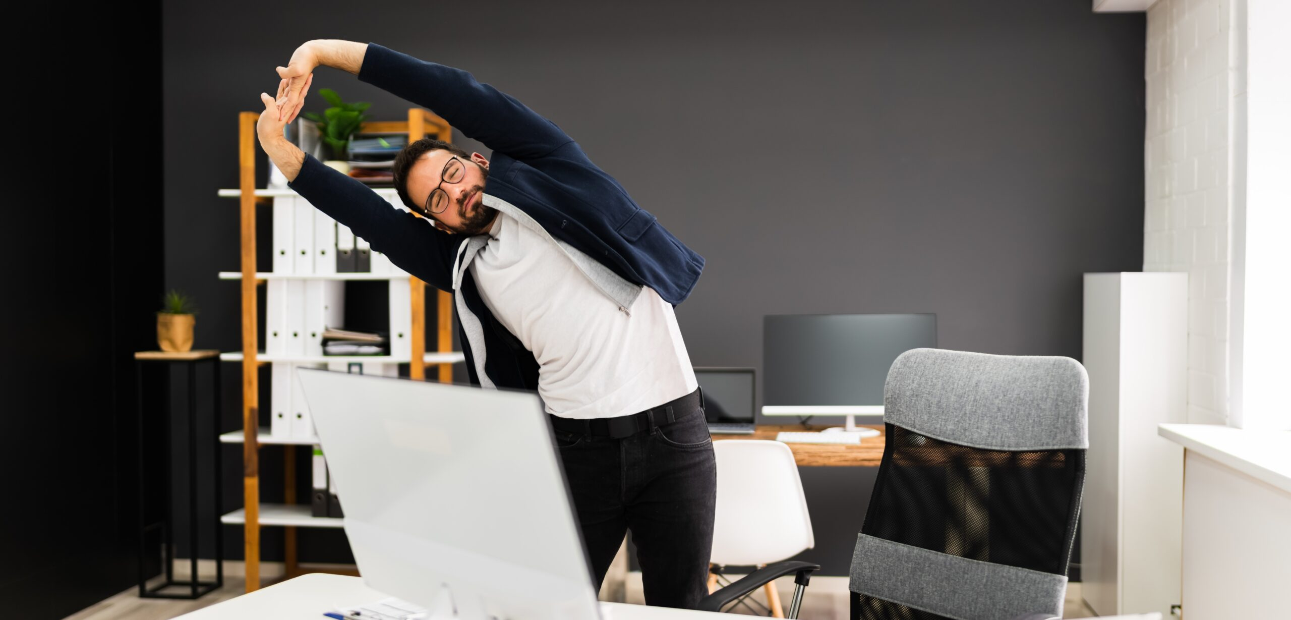 شاب يقف ويمدد جسده في المكتب بعد ساعات من العمل 