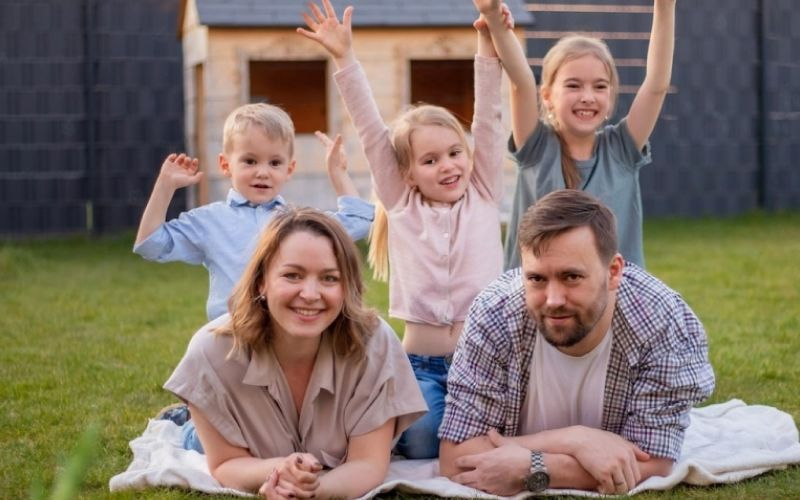 عائلة من اب وام و ثلاثة اطفال في حديقة المنزل يجتمعون بفرح 