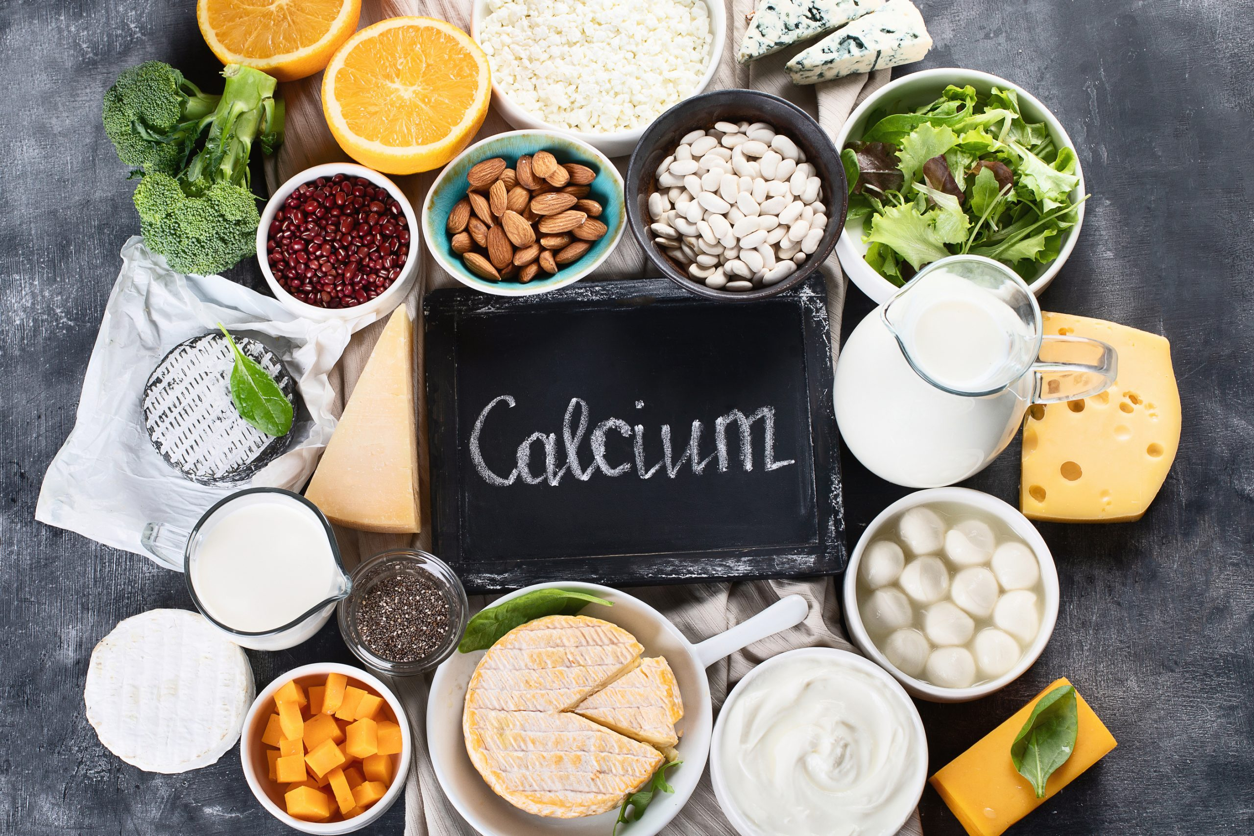 كالسيوم لوح خشبي مكتوب عليه CALCIUM وحوله اغذية غنية بالكالسيوم مثل اللبنة و الجبنة واللوز والحليب و غيرها