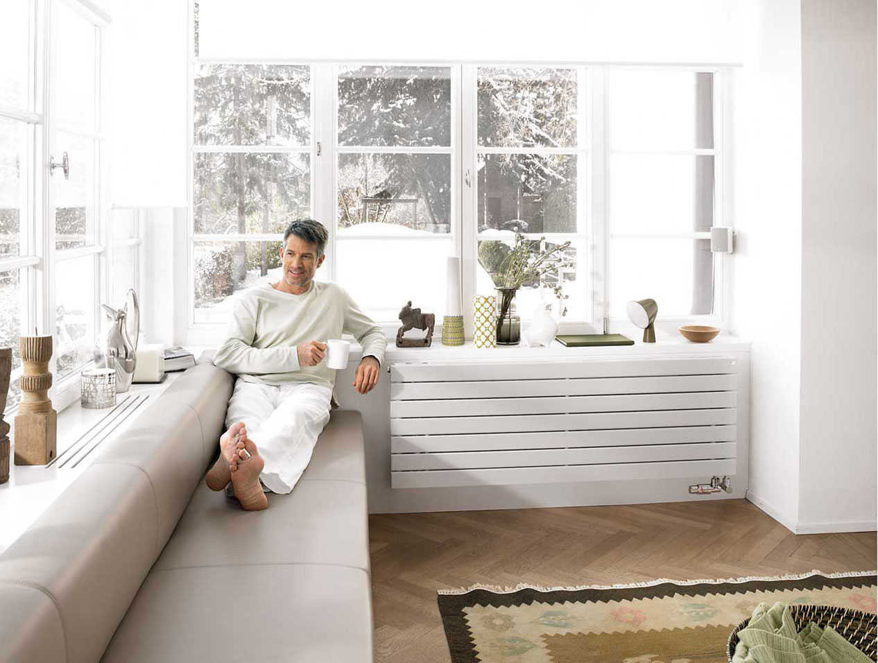 شاب يجلس ممدا رجليه على الصوفا بجانب النوافذ يحتتس مشروب ساخن و يتأمل الثلح المتساقط من النفاذه