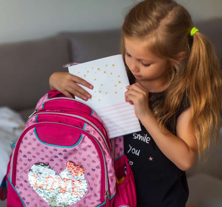 فتاة صغيرة تحضر حقيبة مدرستها الزهرية و تضع دفتر ابيض فيها 