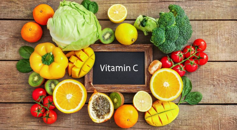 فيتامين سي لوح خشبي مكتوب عليه VITAMIN C وحوله اغذية غنية بفيتامين سي مثل الليمون و الفليفلة و الملفوف والبندورة و غيرها