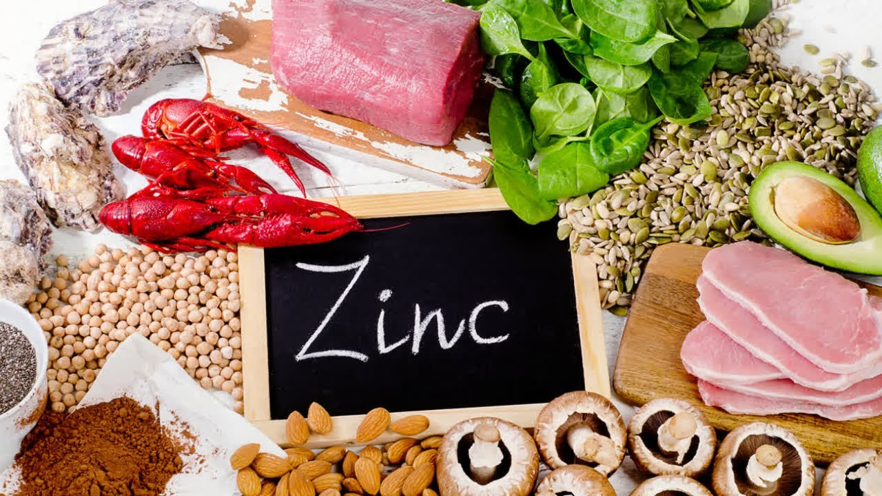 الزنك لوح خشبي مكتوب عليه Zinc وحوله اغذية غنية بالزنك مثل الحمص و الفطر و الافوكادو و بذور اليقطين و اللوز والسمك واللحم الاحمر و القريدس وغيرها