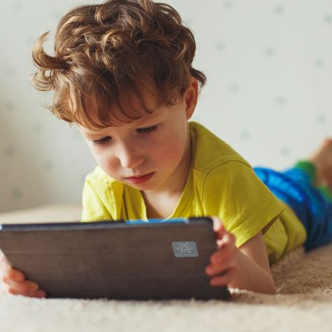 طفل صغير ممسك بيده تاب و يتابع برنامج على شاشته