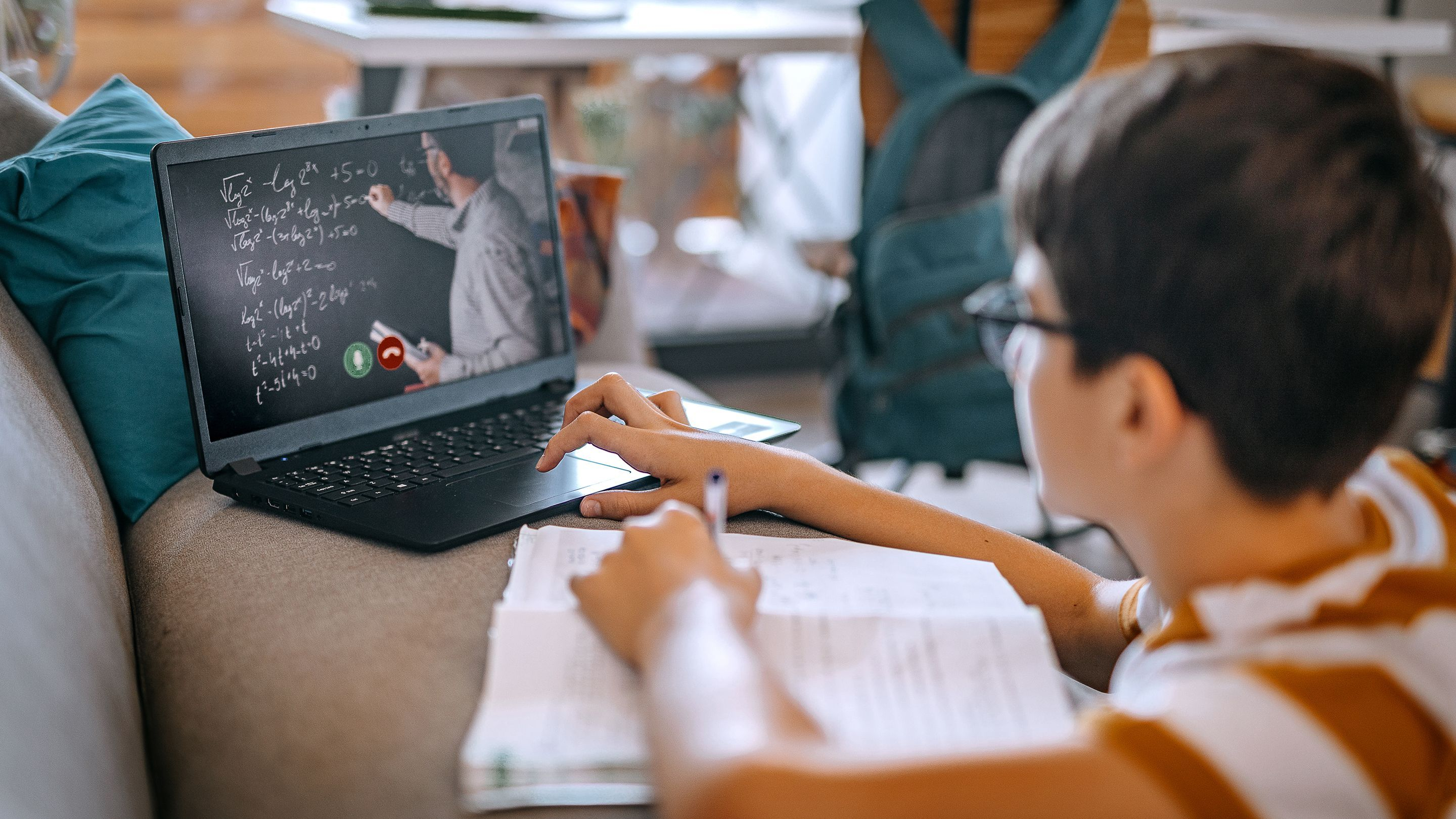 طالب في المنزل يستعمل اللابتوب و يتعلم عن بعد حيث يظهر على الشاشة المعلم  يلقي الدرس 