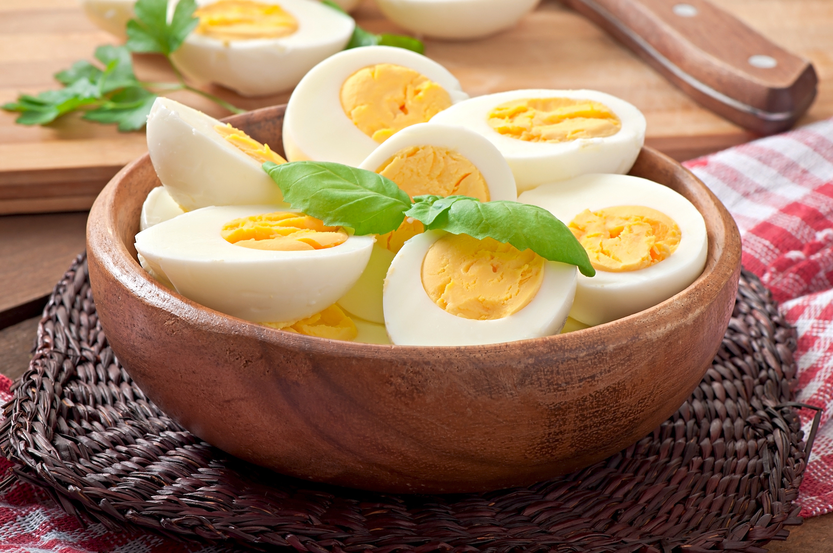 بيض على طبق من القش يوجد طبق من الخشب بداخله بيض مسلوق و مقسوم الى نصفين و عليه ورقتين من النعنع