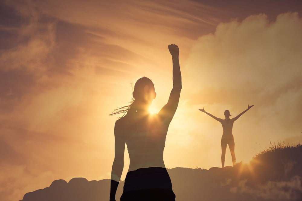 في لحظة الشروق تقف سيدة رافعة يدها كعلامة للانتصار و فتاة اخرى تقف على قمة اعلى ترفع يديها دليل النجاح 