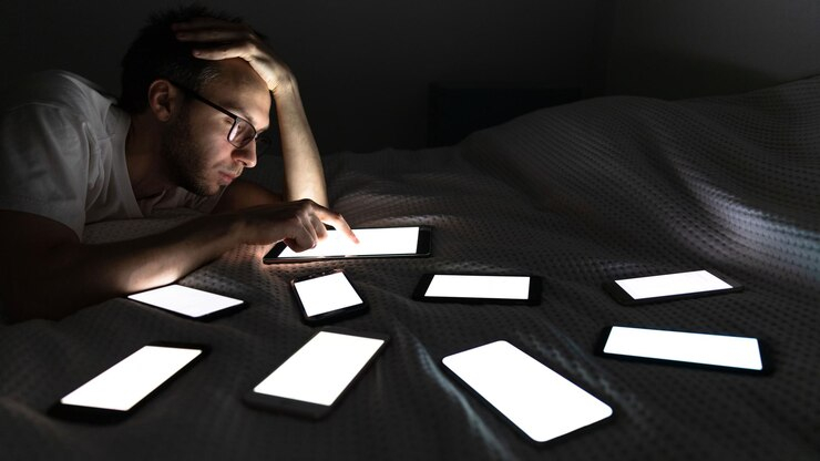 شخص يجلس في الظلام و يتصفح عدد كبير من الموبايلات 