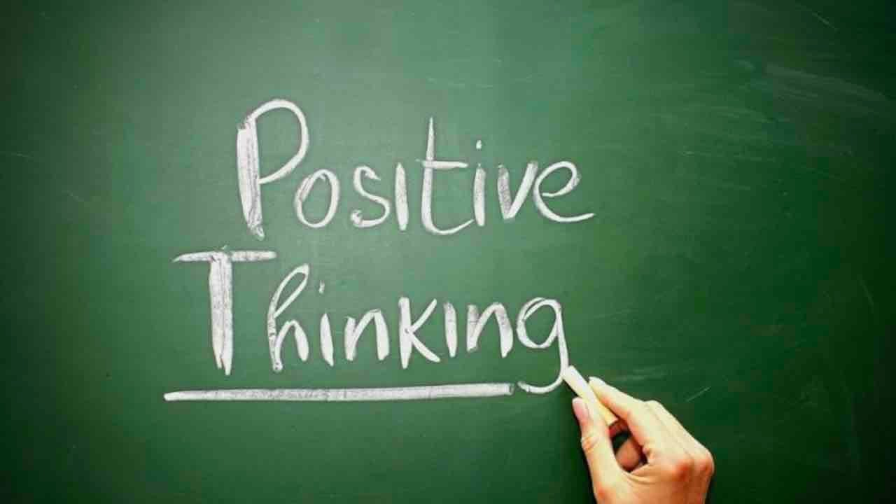 على لوح زيتي تظهر يد تحمل قلم وعبارة مكتوة باللون الابيض positive thinking 