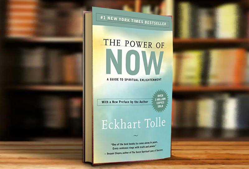 كتاب قوة الآن  على خلفية مكتبة مليئة بالكتب يظهر كتاب قوة الآن موضوع بشكل عامودي