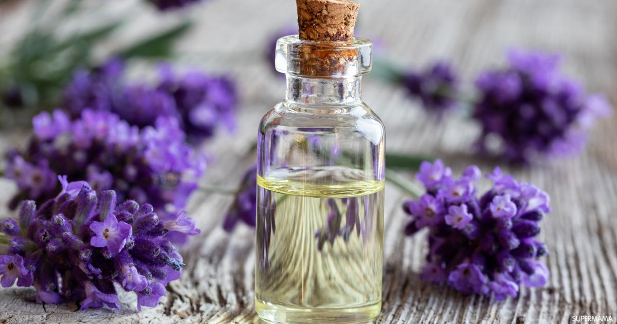 على ارضية من الخشب تظهر عبوة زجاجية تحوي زيت الخزامى و على جانبيه زهر الخزامى أو اللافندر 