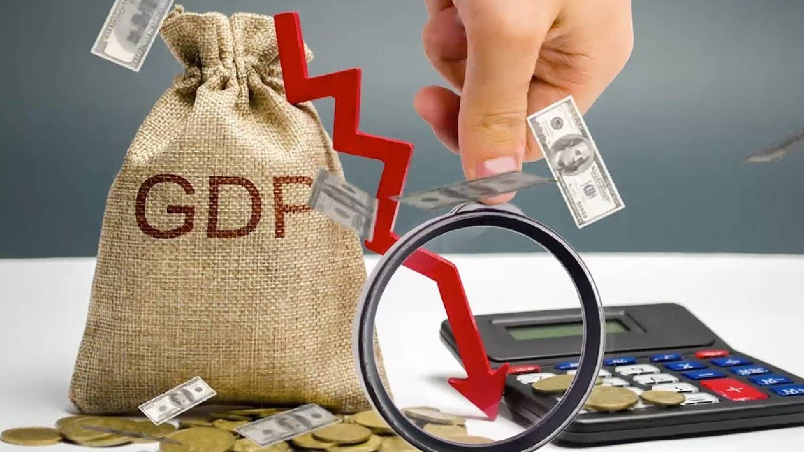 على طاولة يظهر كيس مكتوب عليه GDP وبجانبه نقود ويظهر سهم احمر يتجه للاسفل و بجانبه آلة حاسبة و يد ممدودة وبجانبها اوراق نقدية