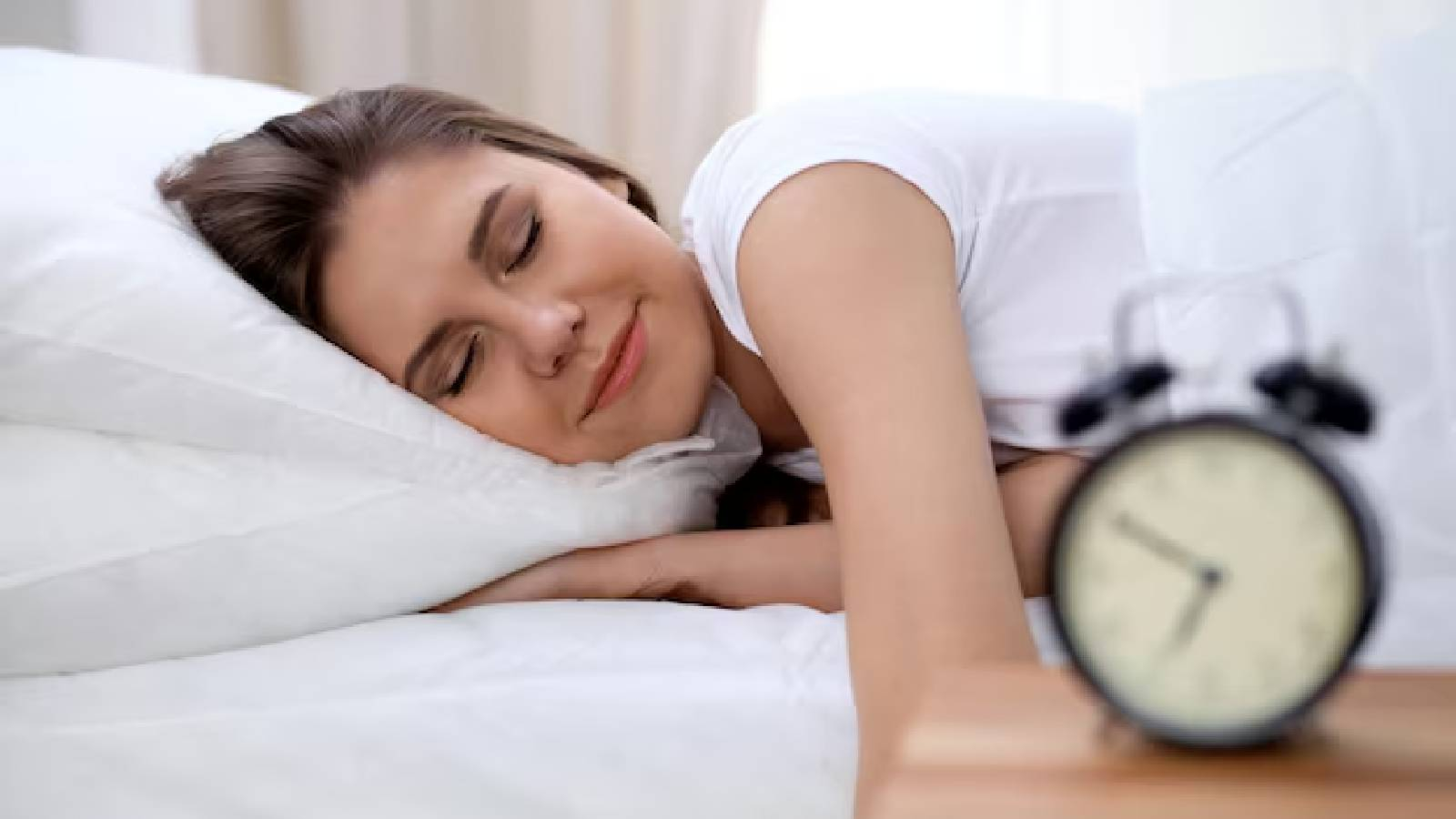 سيدة تغط في نوم عميق على سرير ابيض و بجانبها ساعة منبه 