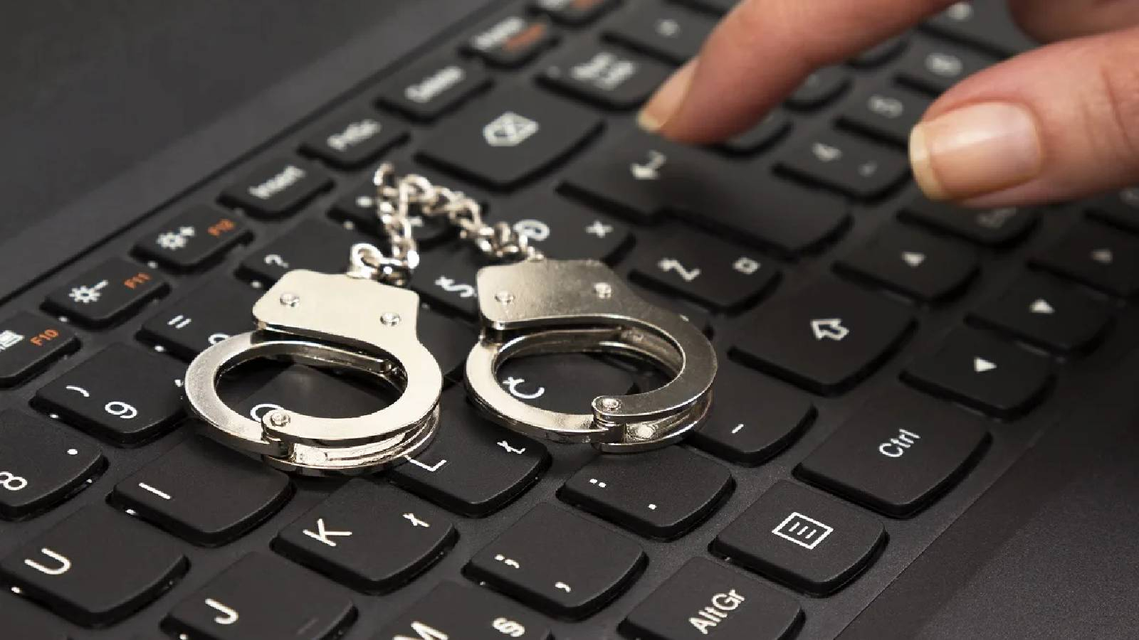 على لوحة مفاتيح جهاز كمبيوتر تظهر اصابع شخص و بجانبها اصفاد سجن 