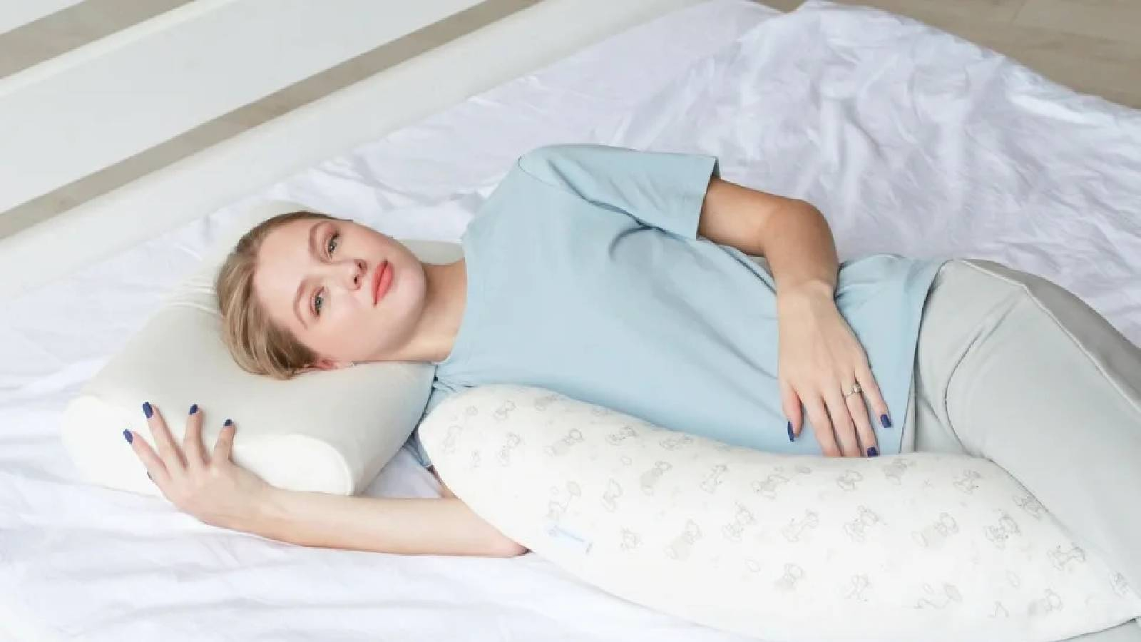 فتاة مستلقية على السرير في وضعية الاسترخاء وهي تضع يدها على بطنها و يدها الثانية تحضن المخدة 