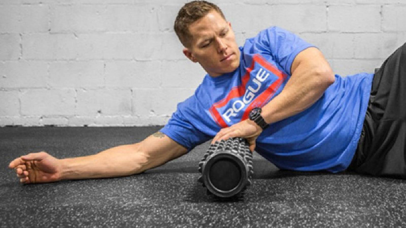 شاب يمارس تمارين الكاريدو من خلال التمدد على جانبه و تحت ابطه اسطوانة تساعده على التمدد 