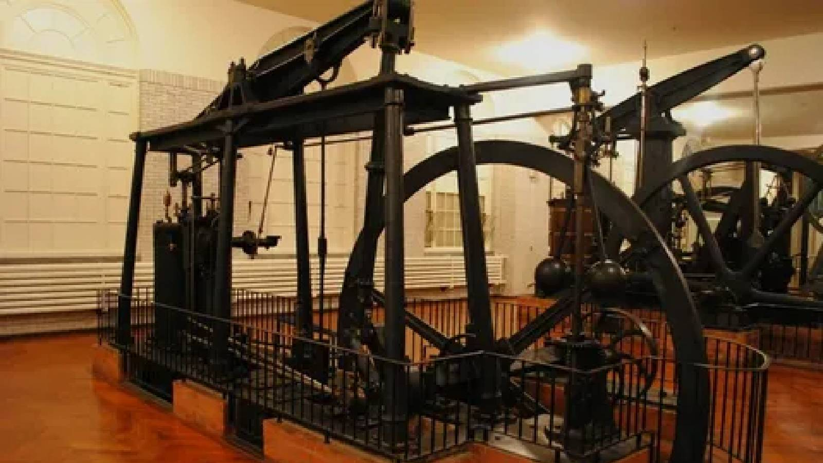  ضمن قاعة عرض يظهر محركات بخارية من  اختراع جيمس واط حيث تظهر عجلة كبيرة و رافعة مع بعض الاعمدة الفولاذية موضوعة ضمن سياج من الحديد ويظهر 