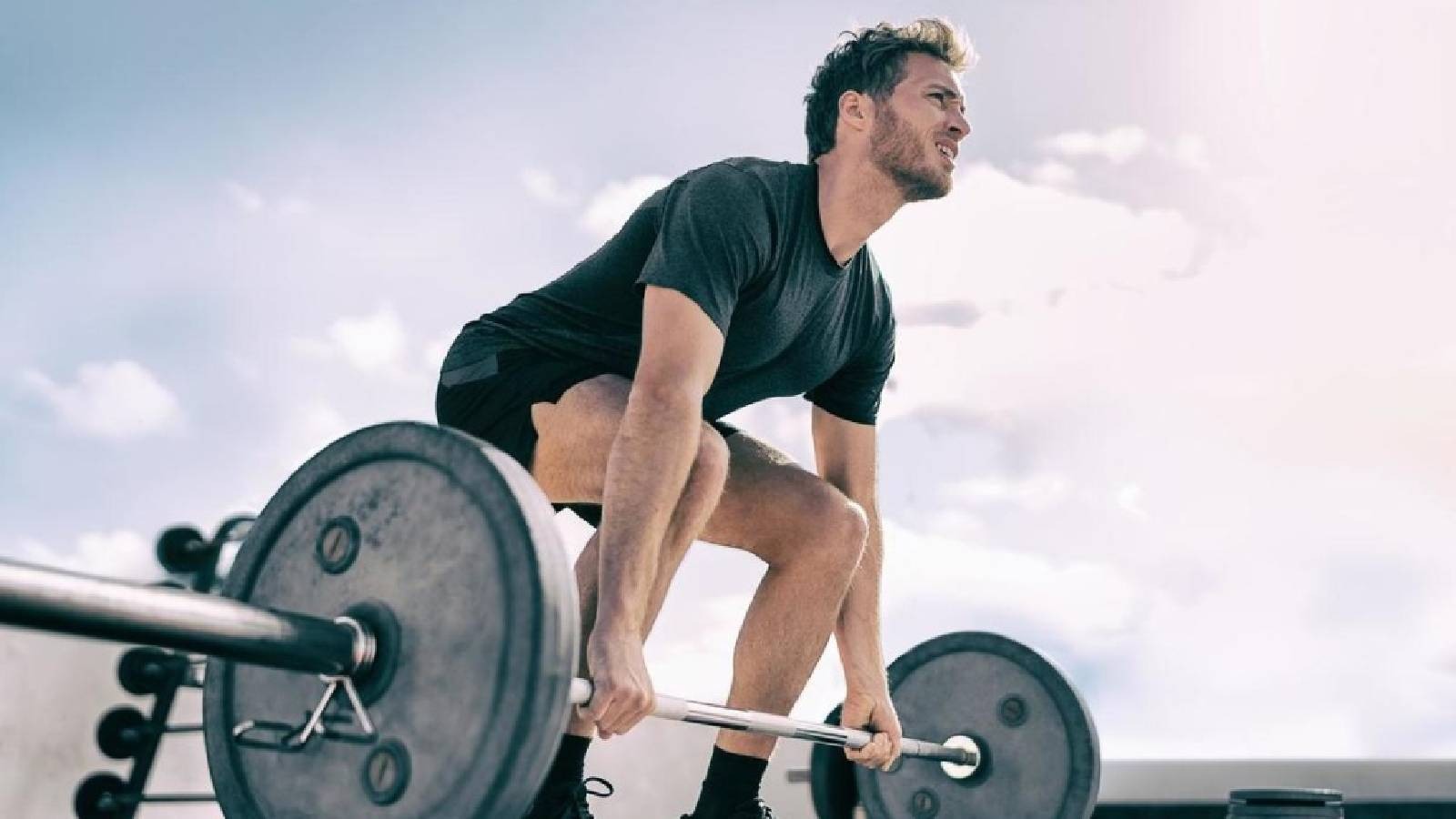 رجل في الهواء الطلق وهو يرتدي تيشيرت وشورت اسود منحني بجسده للامام يمسك بيديه اثقال