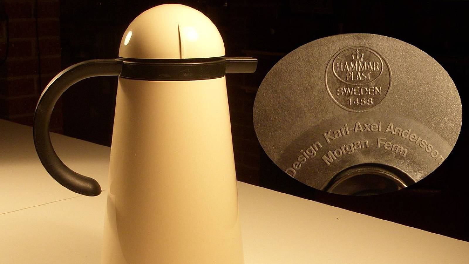 على طاولة لونها كريمي عليها حافظة حرارة للقهوة لوناه كريمي ذات مقبض بني و بجابنها دائرة بلون الشوكرولا مكتوب بداخلها Hammarplast