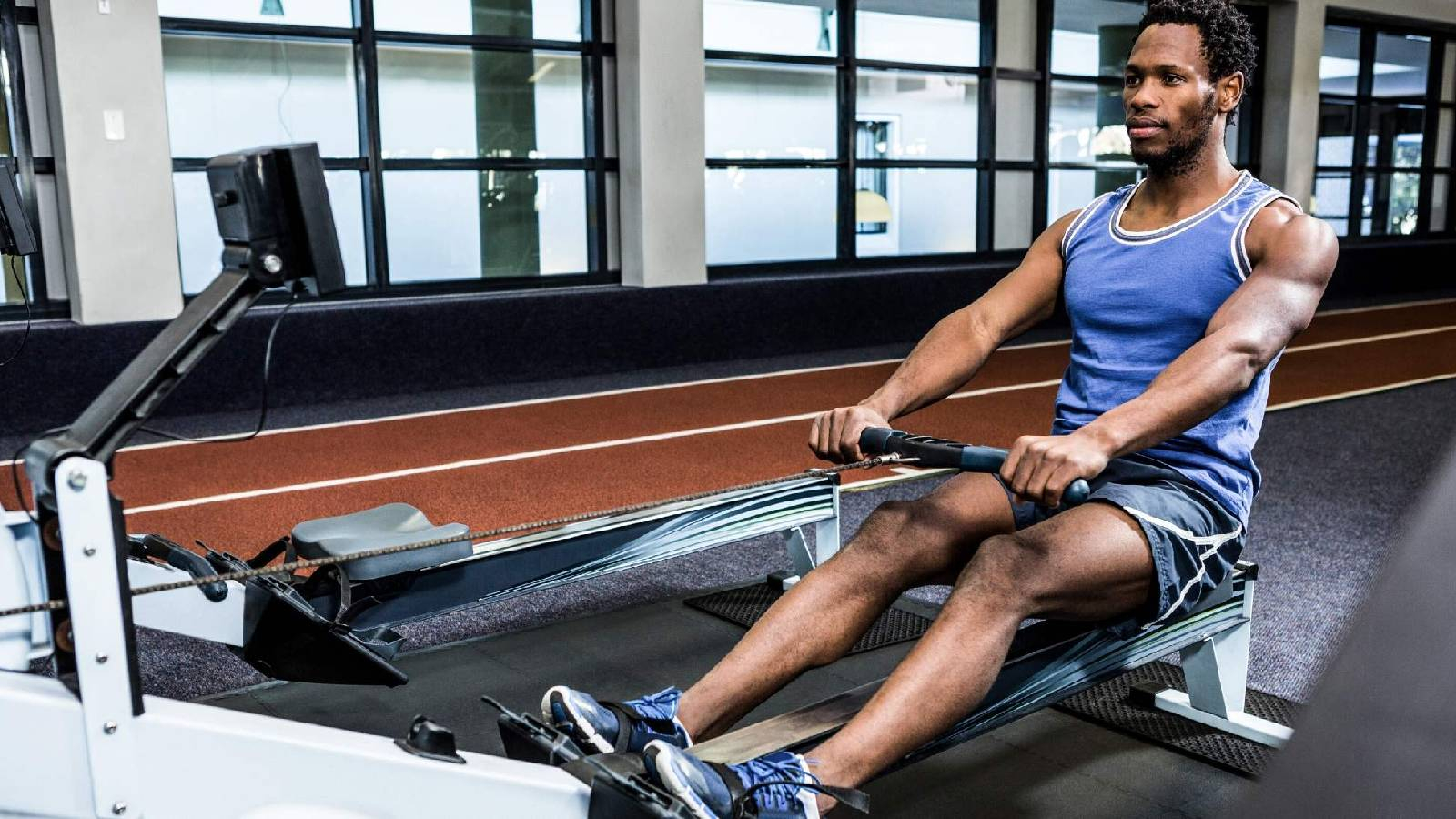 رجل في النادي الرياضي و هو يرتدي تيشيرت ازرق و يجلس على كرسي التمرين و هو يسحب الاثقال من الامام بشكل افقي 