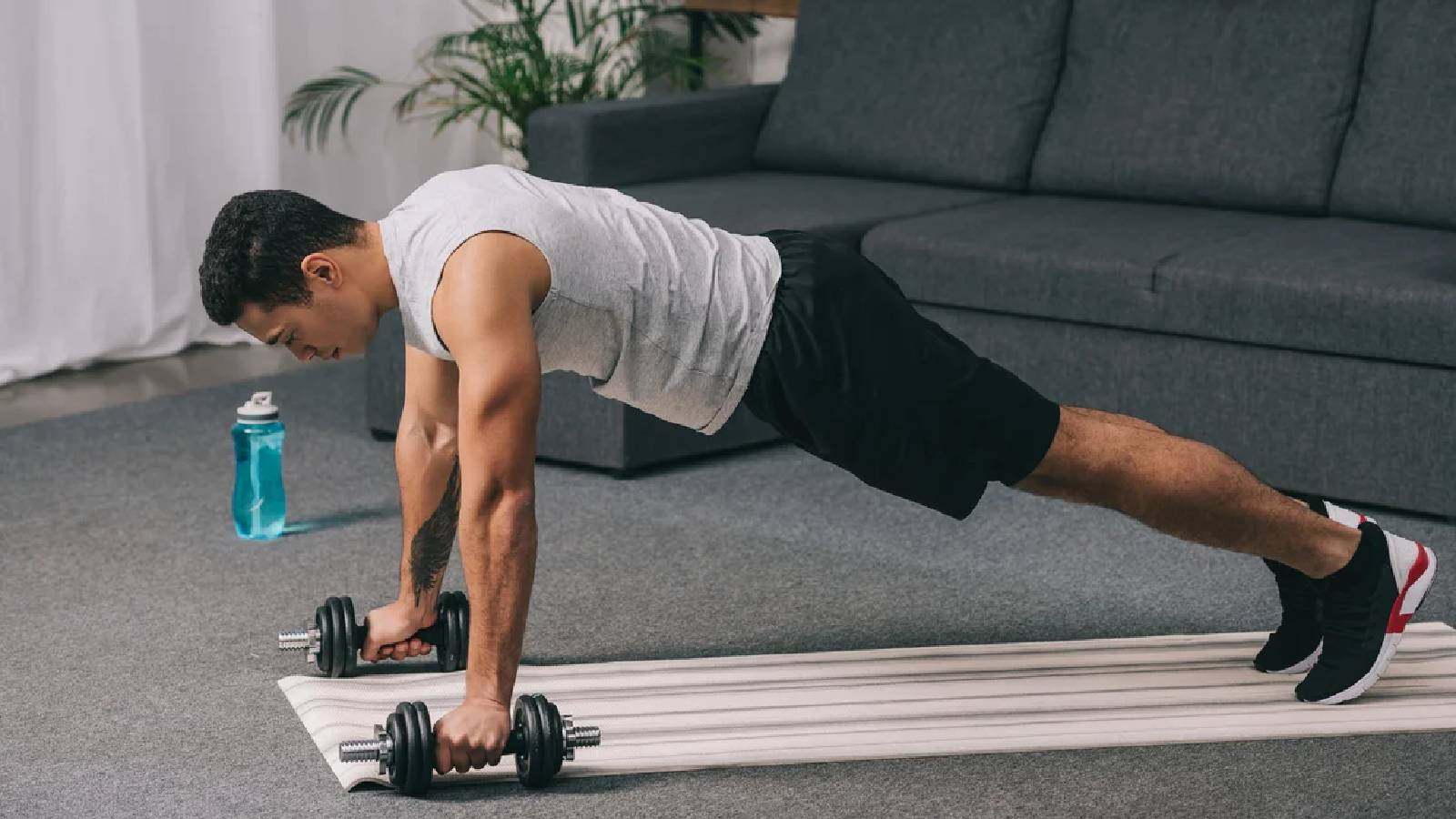 رجل يرتدي تيشيرت رمادي و شورت اسود وهو يمارس تمرين البلانك ويستند على الاوزان 