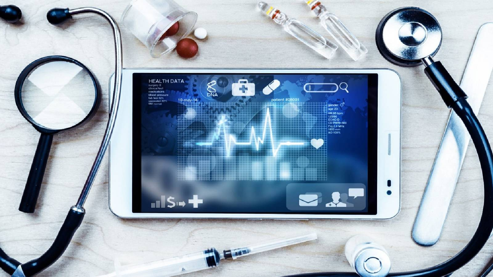  على طاولة بيضاء تظهر ادوات تطبيق متابعة طبية لدقات القلب والمؤشرات الحيوية من سماعة و ادوية و في الوسط جهاز هاتف ذكي تظهر على شاشته  المؤشرات الحيوية 