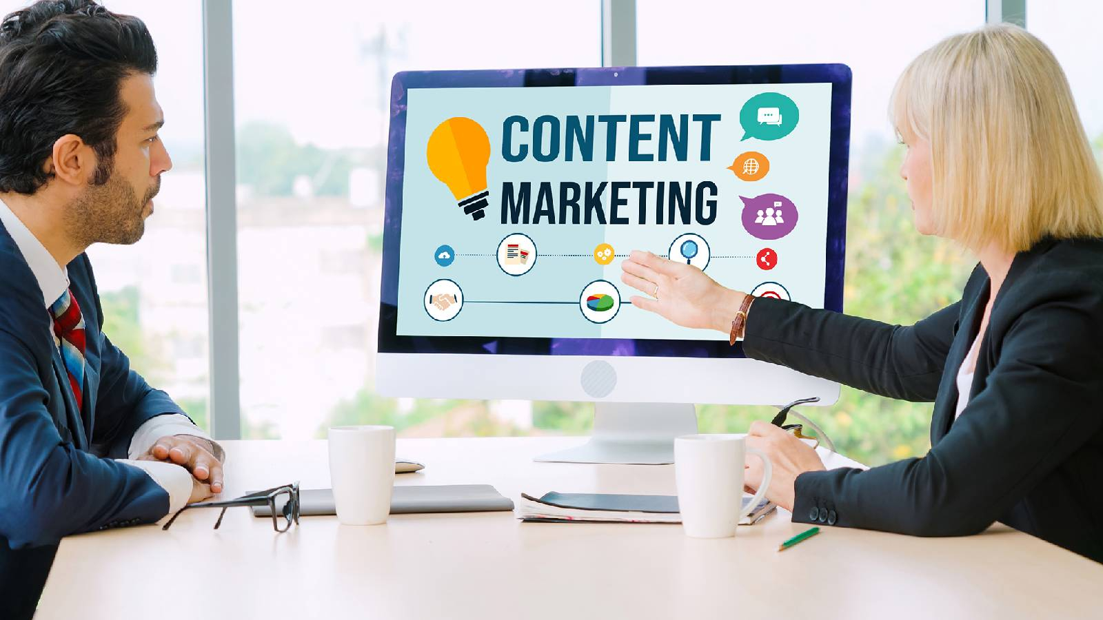 رجل وسيدة يجلسون الى طاولة اجتماع و تشير السيدة الى شاشة كومبيوتر تظهر على شاشته عبارة content marketing 
