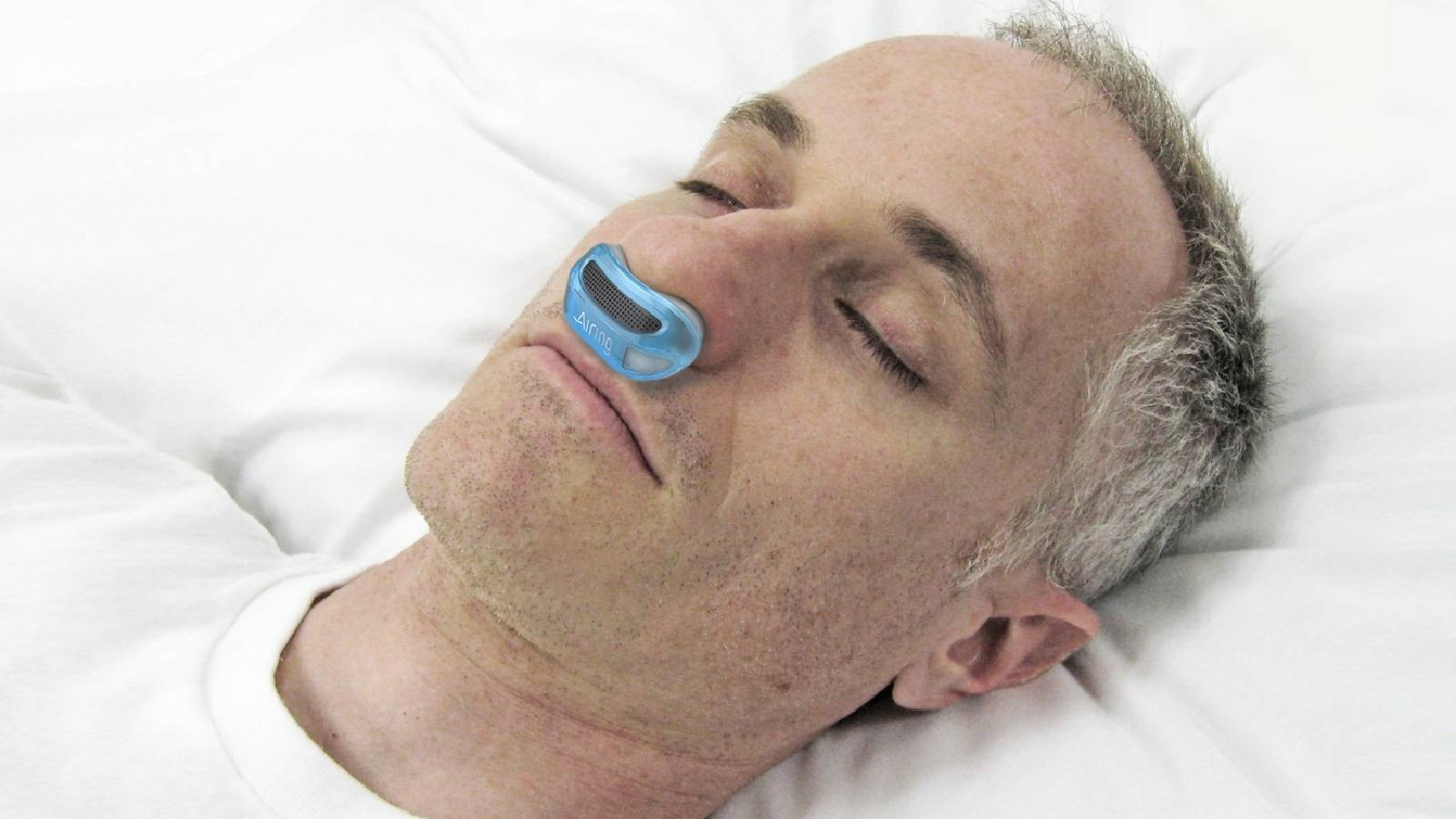 شخص نائم على وسادة بيضاء و يضع في انفه جهاز يمنع الشخير اثناء النوم 