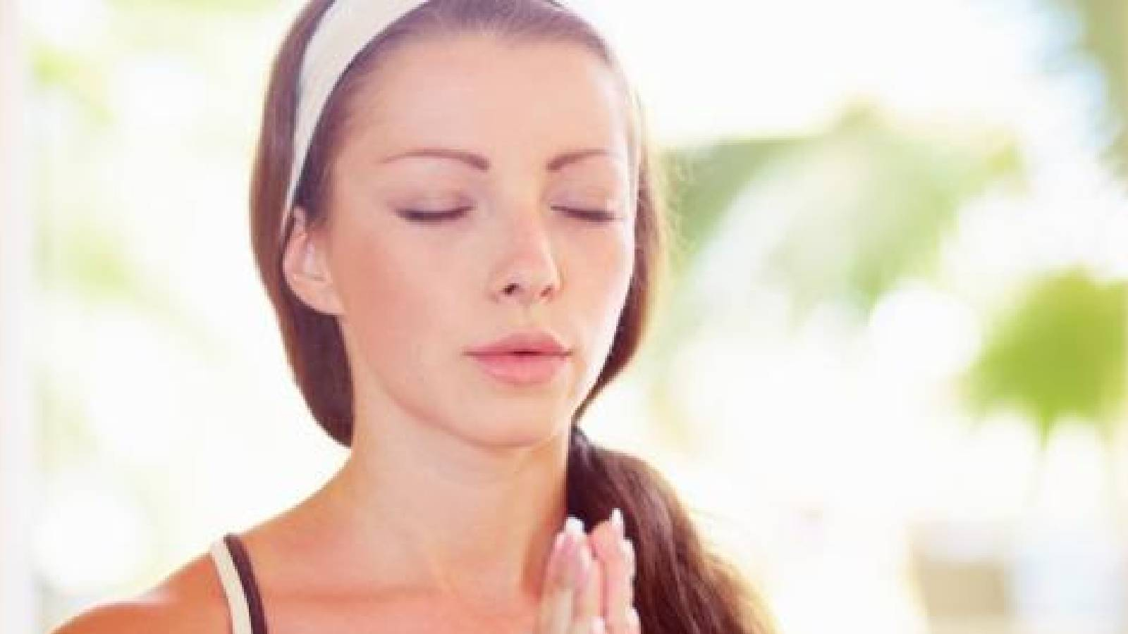 فتاة تضع ربطة على شعرها وتضم يديها وتتنفس بنغمة واحدة و خلفها خيال لبعض اوراق النباتات