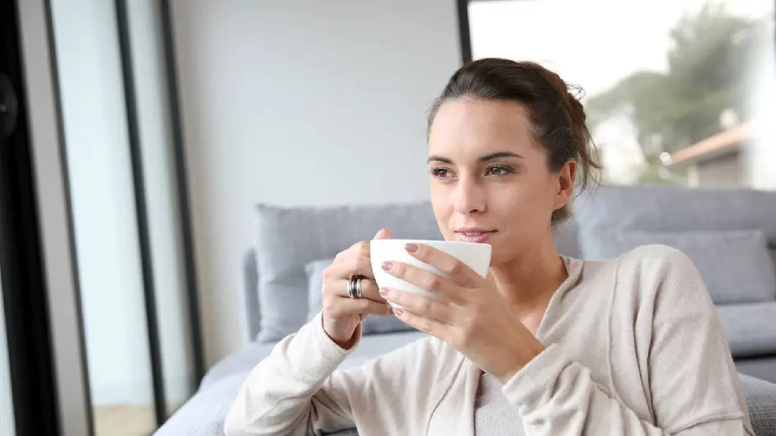 سيدة تتمت بكوب من الشاي وهي تجلس على الاريكة بجانب نافذة غرفتها 