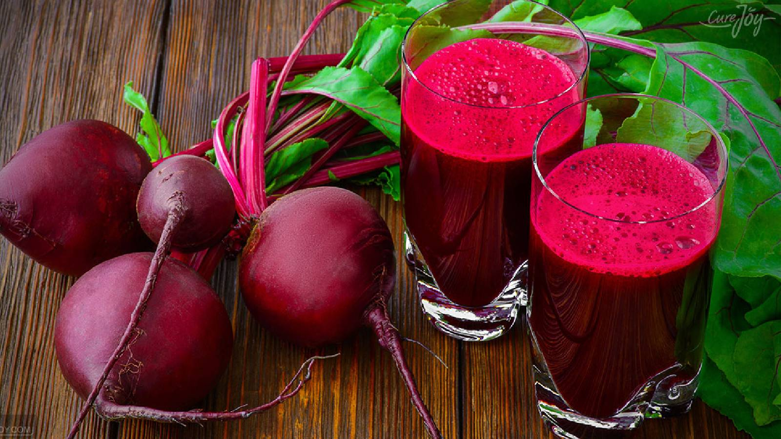 كأسين من عصير الشوندر بجانبه حبات من الشوندر واراقها الخضراء الجميلة 