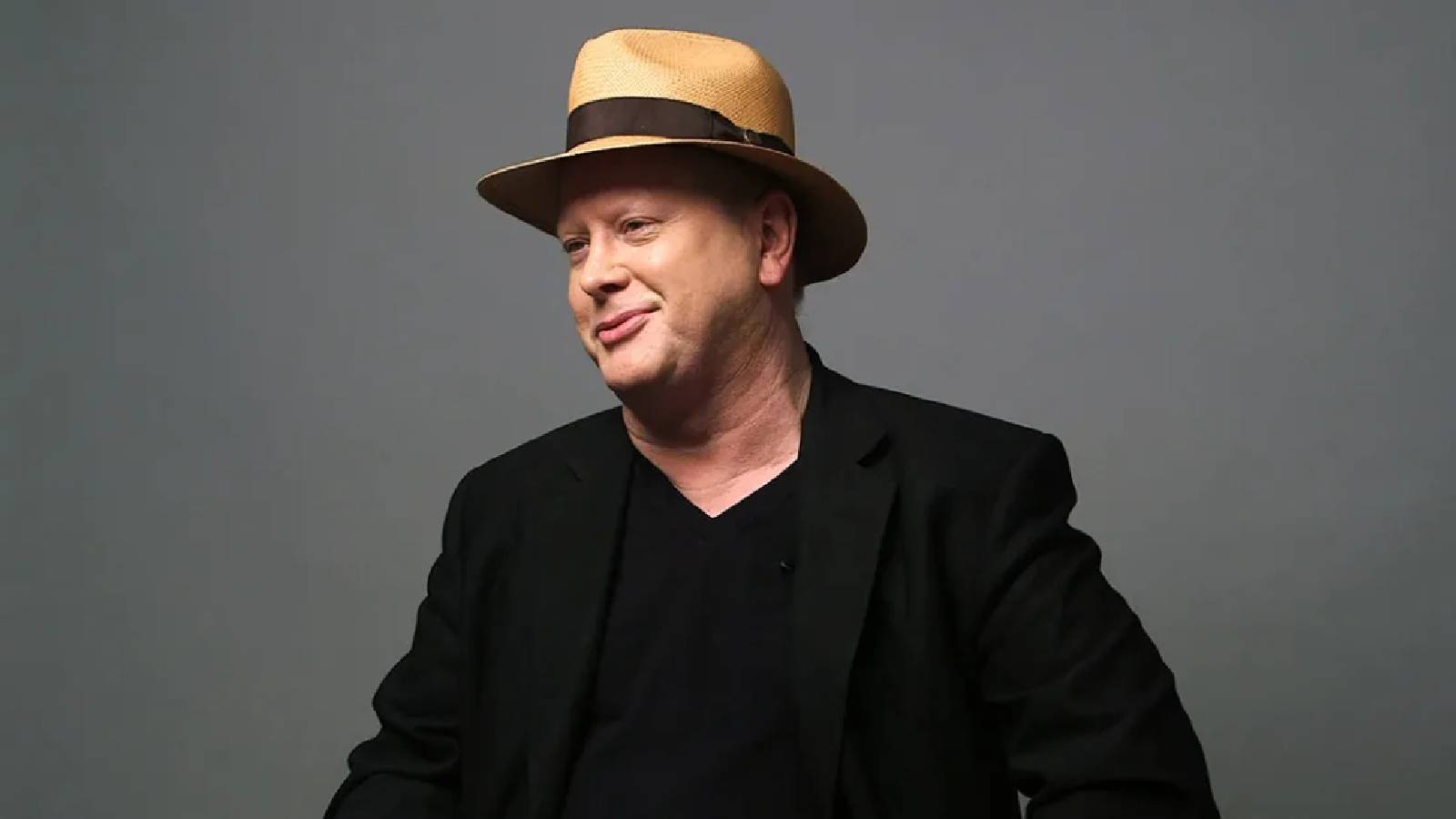 Darrell Hammond يرتدي بدلة سوداء ويضع على رأسه قبعة بنية ذات شريط اسود والصورة بخلفية رمادية 