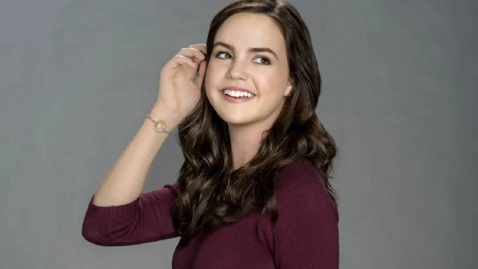 Madison Bailey رمرتدية بلوزة بنفسجية وترفع يدها اليمنى تلملم خصلات شعرها وتضع اسوارا بيدها اليمنى وهي تنظر الى الجهة اليسرى 