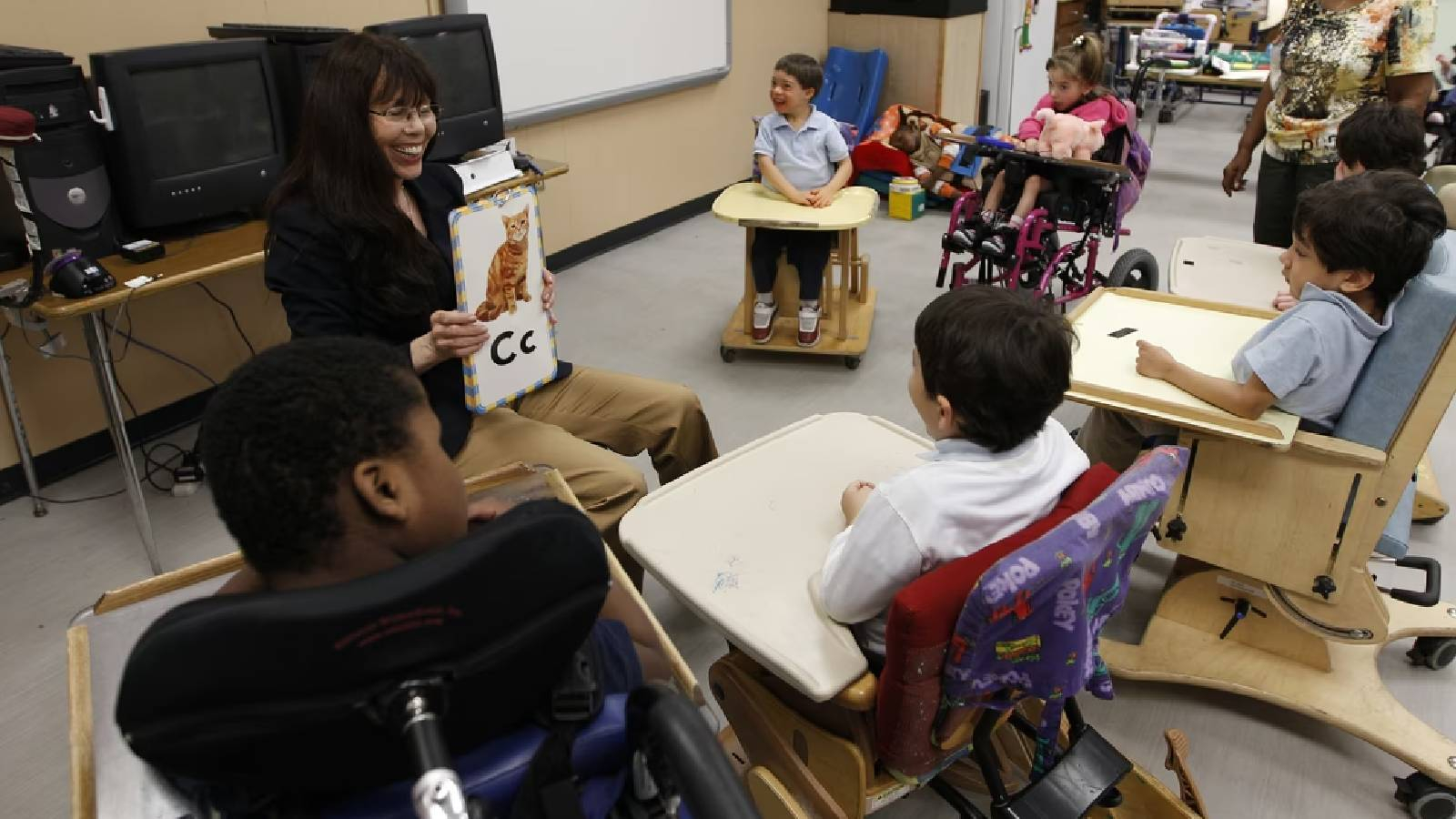 معلمة تجلس في صف لطلاب من ذوي الاحتياجات الخاصة و هم جالسون على كراسيهم الخاصة 