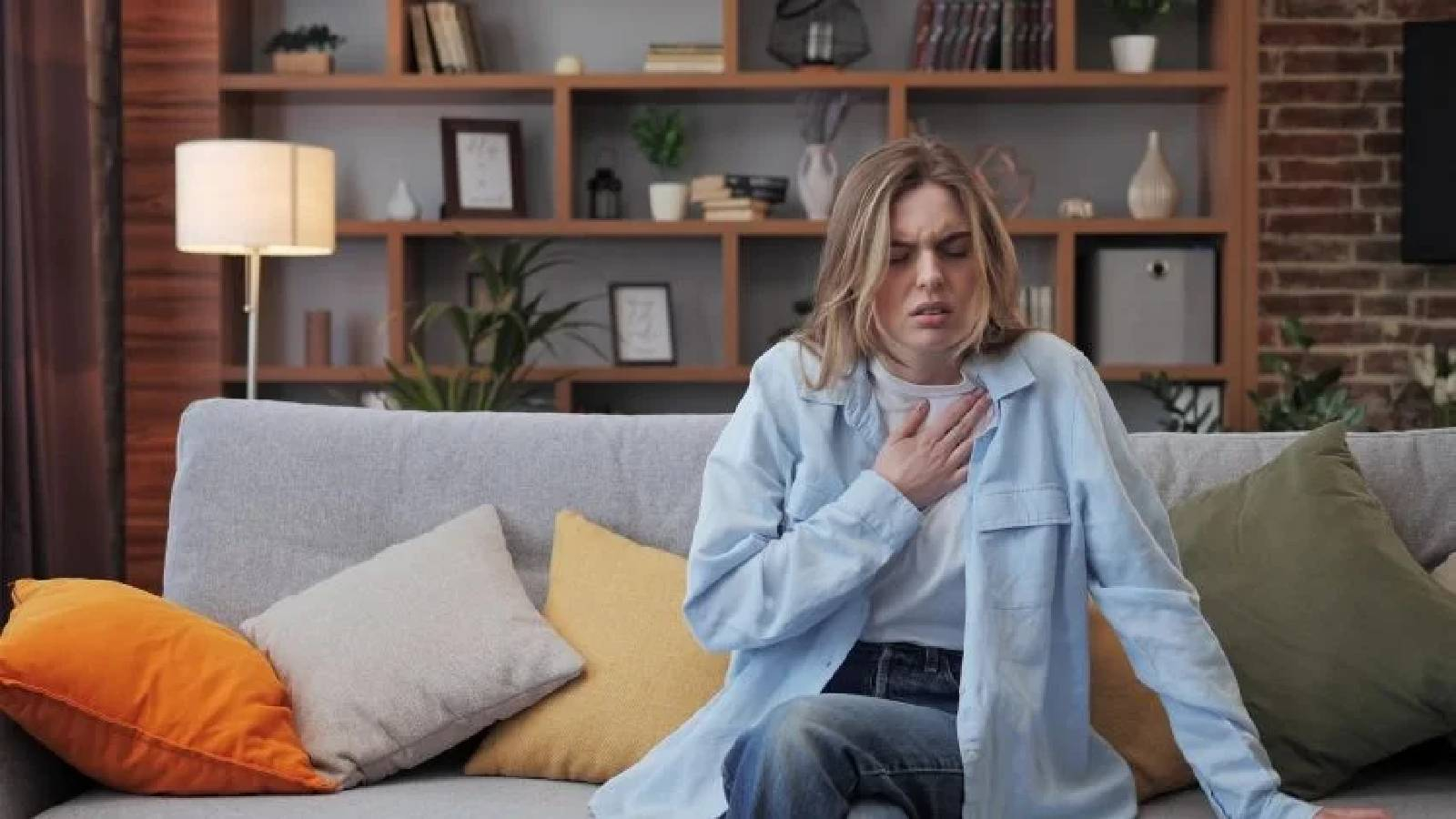 سيدة تجلس على الصوفا في المنزل تضع يدها على صدرها وهي تعاني من متلازمة الابنية المريضة 