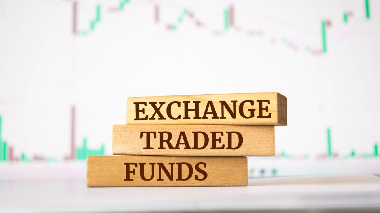 على خلفيه تظهر فيها خطوط بيانية يوجد ثلاث قطع خشبية مستطيلة و مكتوب عليها EXCHANGE - TRADED - FUNDS 