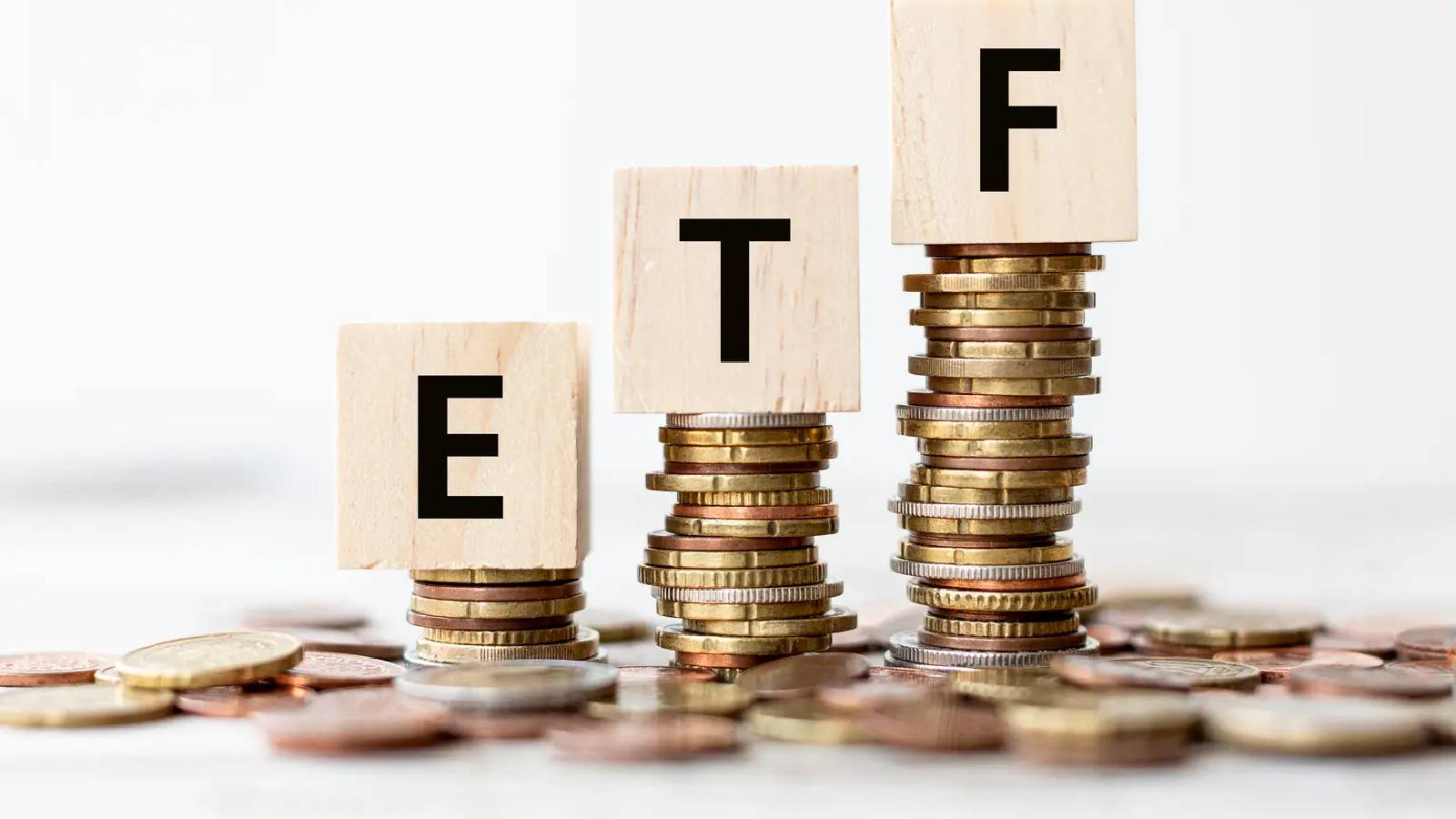 مجموعة من العملات النقدية موضوعة فوق بعضها لتشكل ثرث اعمج و فوق كل عامود يوجد مكعب من الحشب و عليها احرف ETF