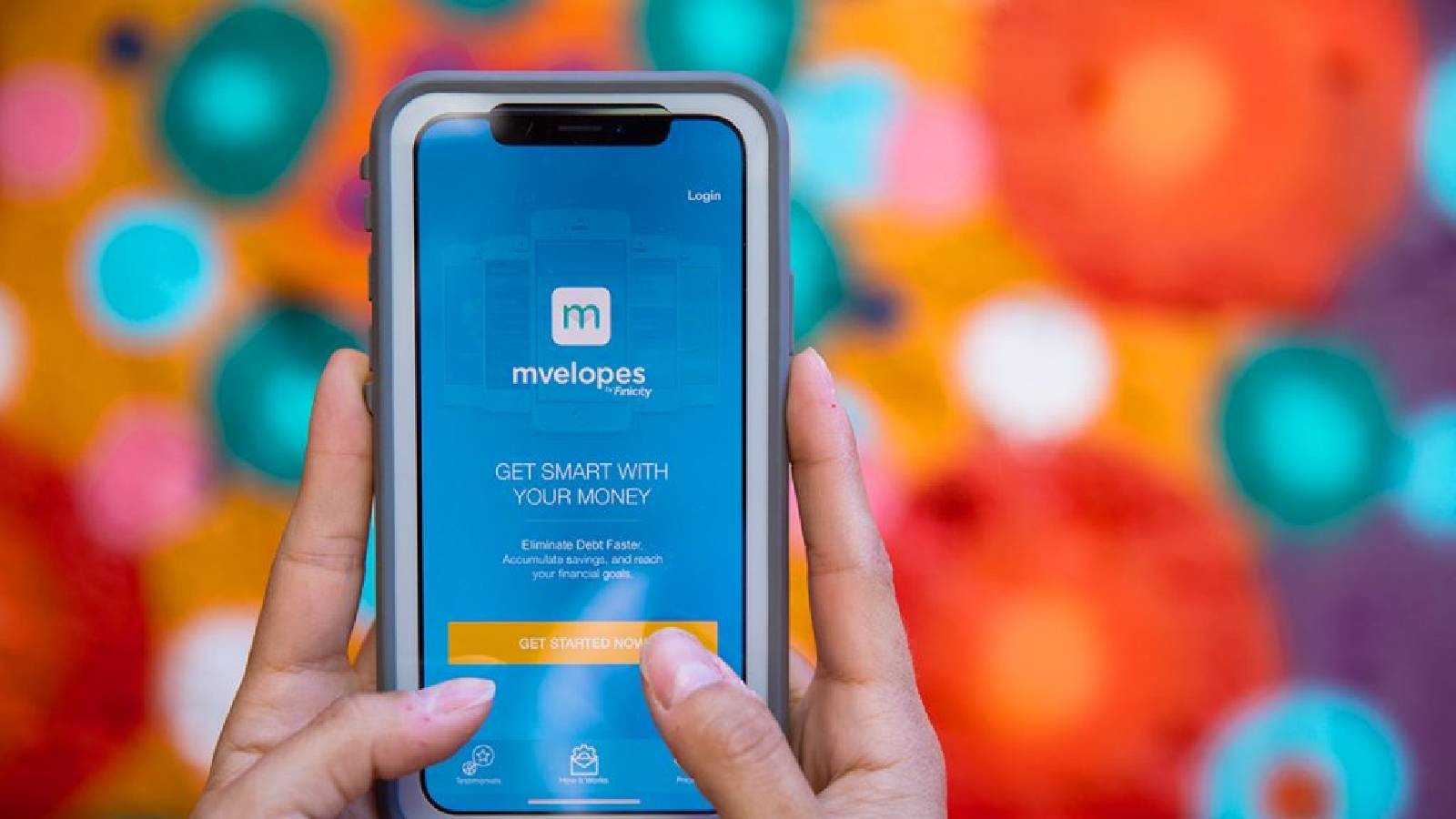 على خلفية ملونة تظهر يدين تمسكان بهاتف ذكي تظهر على شاشته الزرقاء تتطبيق Mvelope