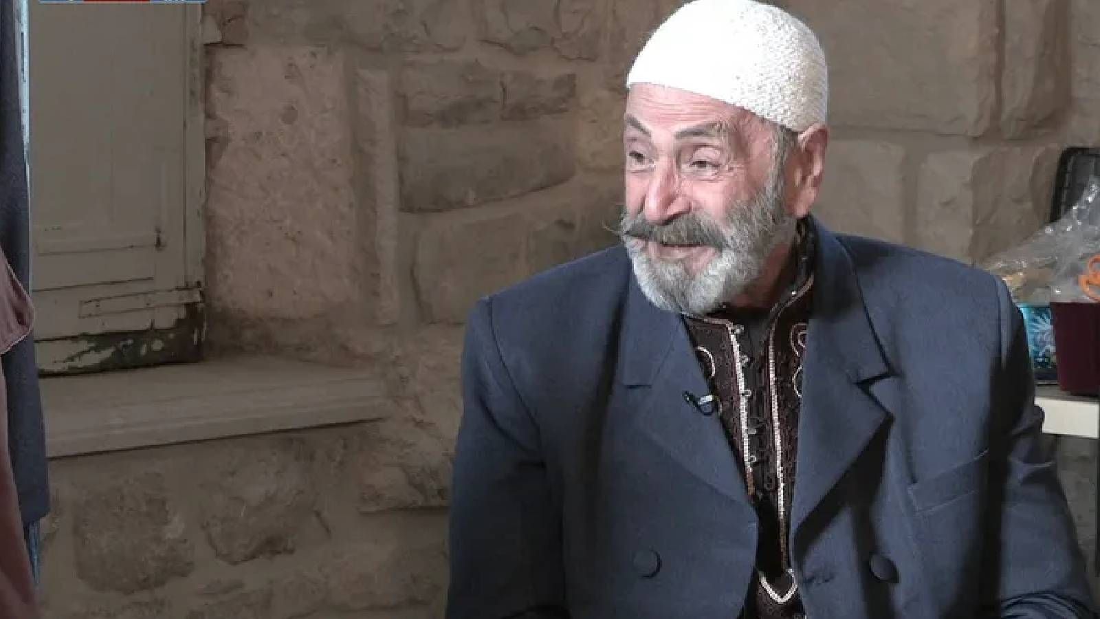 الفنان رفيق السبيعي جالسا بلباسه الدمشقي التقليدي والشعبي ويضع قبعة شعبية بيضاء 