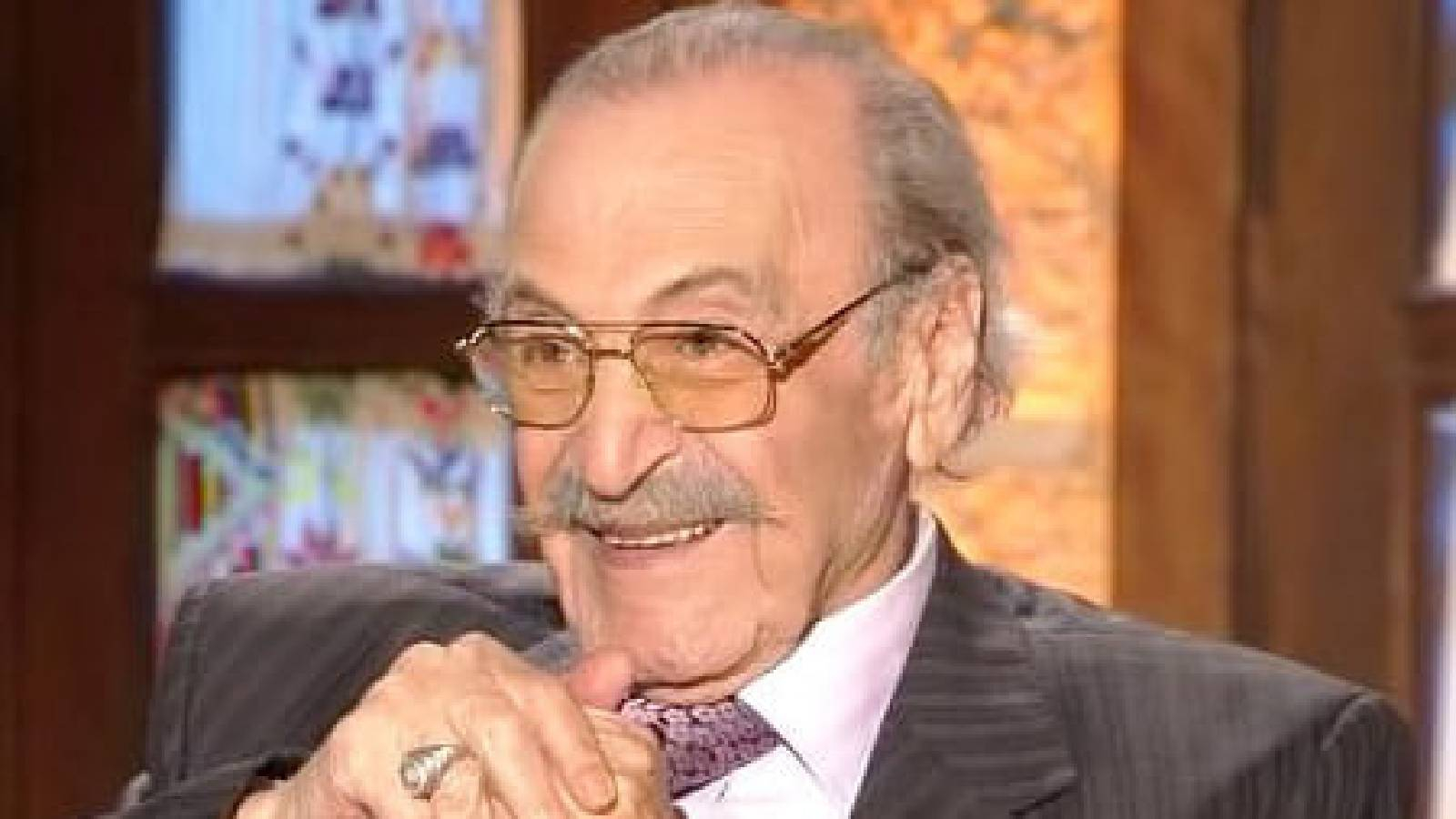 الفنان رفيق السبيعي في لقاء تلفزيوني وهو يشبك يديه مبتسما