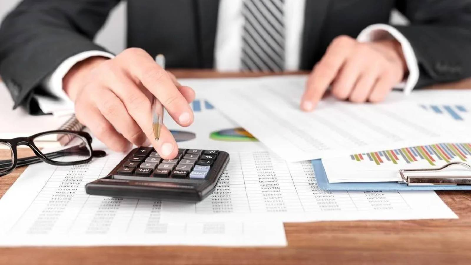 محاسب يعمل على تدقيق مجموعة من التقارير مستخدما آلة حاسبة 