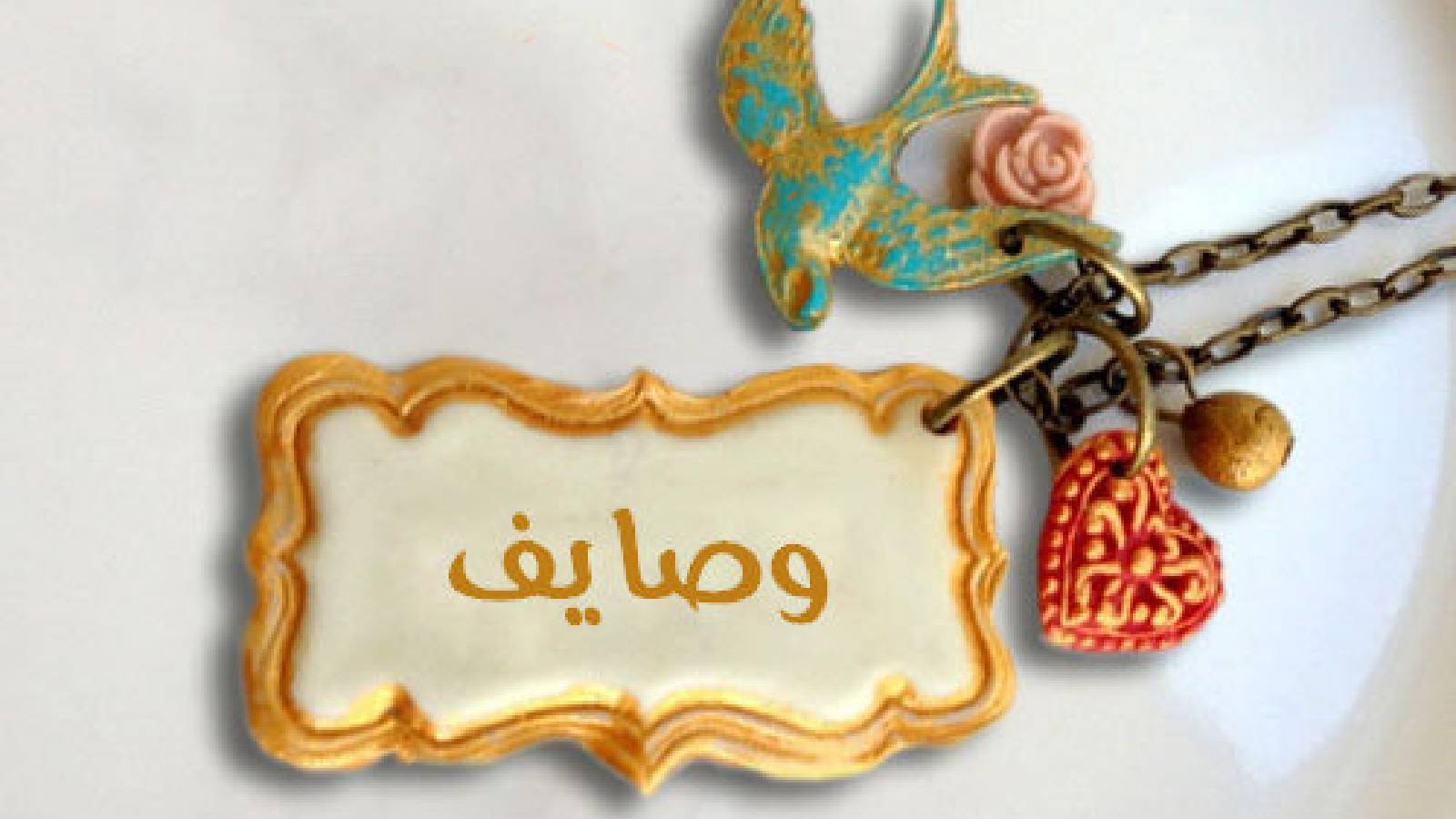 قلادة يحوي قلب احمر و عصفورة و قطعة مستطيلة في وسطها مساحة بيضاء مكتوب في وسطها اسم وصايف 