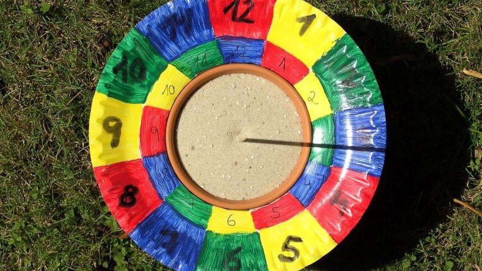 ساعة شمسية مصنوعة من صحن من الكرتون مقسم الى اقسام ملونة تدل على الساعات و في الوصط عصى ينعكس ظلها على الصحن لتدل على الساعة 